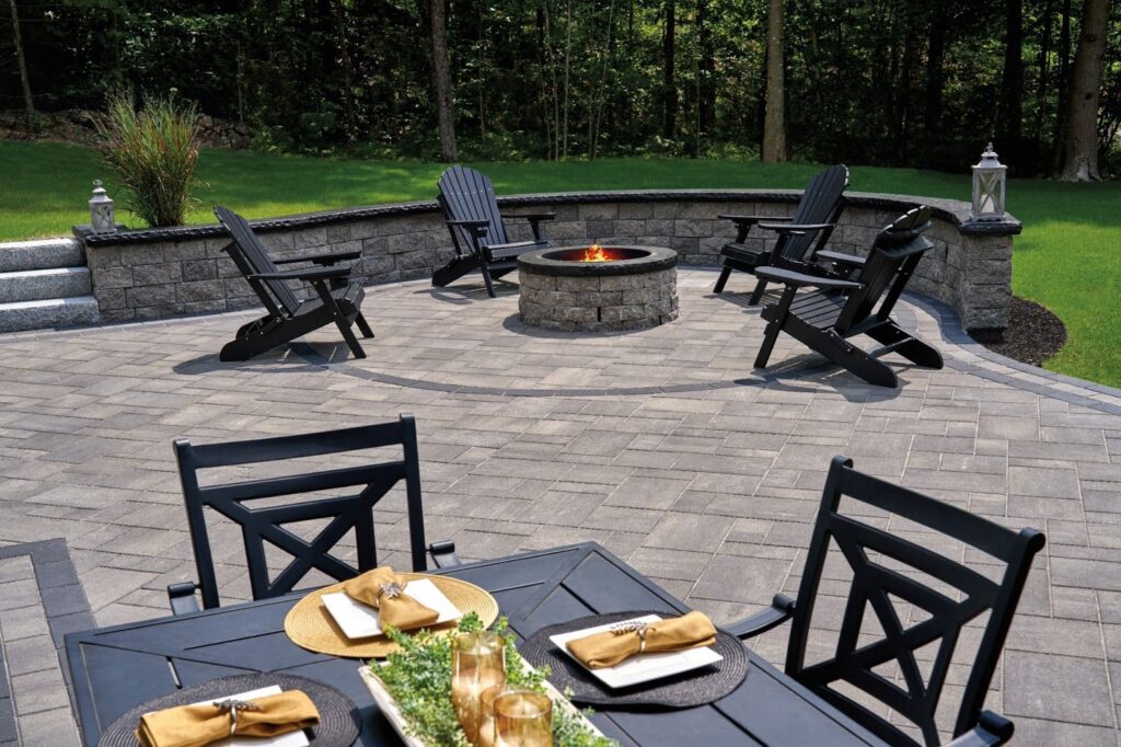 An outdoor living space with black patio furniture set on a natural stone patio, bordered by a stone retaining wall and landscaped grass.